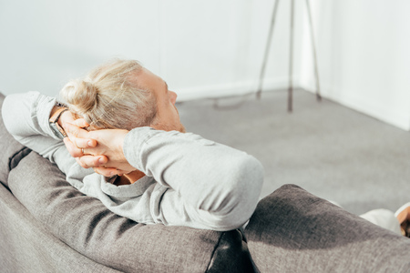 back view of man resting with hands behind head on couchの写真素材