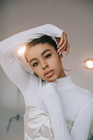 beautiful african american female model in white turtle neck looking at camera in studio with spotlightsの写真素材