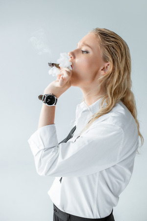 beautiful fashionable young woman smoking cigar isolated on greyの写真素材