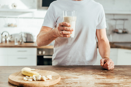 cropped shot of athletic man holding glass with banana protein shake at homeの写真素材