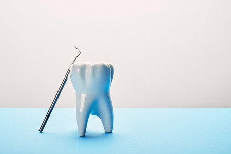 close up view of tooth model and dental probe on blue and white background
