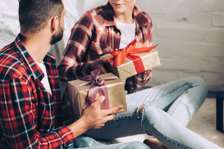 cropped image of couple in checkered shirts giving christmas presents to each other at homeの写真素材