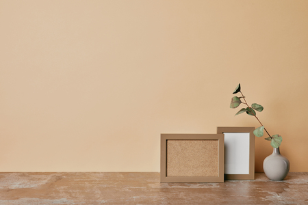 Two photo frames and vase with flower on table on beige backgroundの写真素材