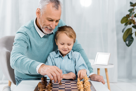 smiling middle aged man teaching grandson to play chess at homeの写真素材