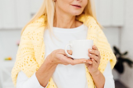 close up of blonde woman holding white cup at kitchenの写真素材