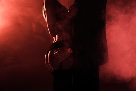 Partial view of attractive seductive couple in hug on red smoke backgroundの写真素材