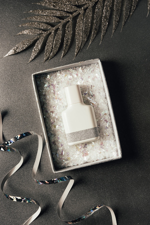 top view of perfume bottle in box, silver ribbons and shiny decorative leaves on greyの写真素材