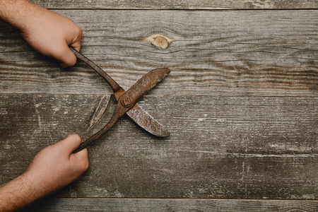 Partial view of worker holding vintage rusty carpentry scissors on wooden backgroundの写真素材