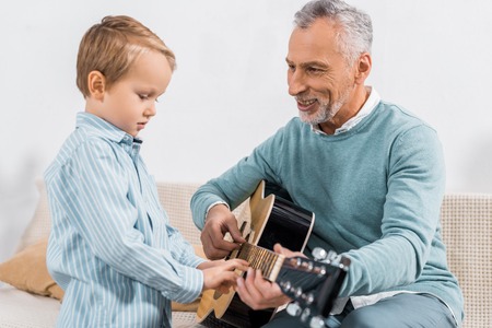smiling middle aged man teaching grandson playing on acoustic guitar at homeの写真素材