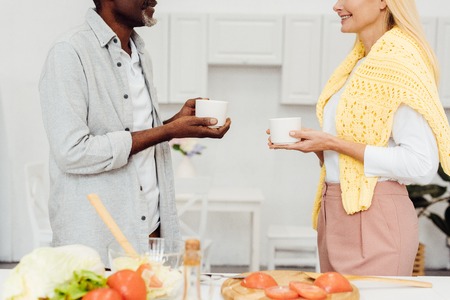 cropped view of mature blonde woman and african american man drinking coffee together at kitchenの写真素材