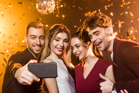 group of happy friends taking selfie with smartphone during party