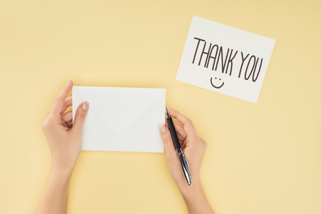 cropped person holding pen and blank sheet of paper, white postcard with thank you lettering isolated on yellow backgroundの写真素材