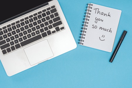 laptop, pen and notebook with thank you so much lettering isolated on blue backgroundの写真素材
