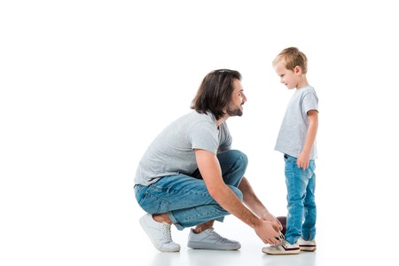 Caring father helping his son to tie shoelace isolated on whiteの写真素材