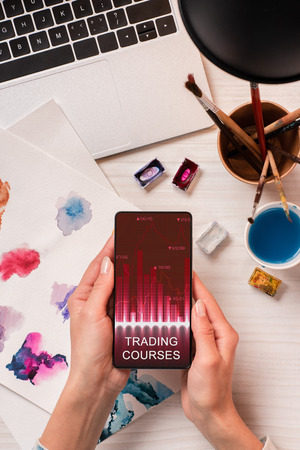 cropped view of designer at office desk holding smartphone with graph on screen, flat layの写真素材