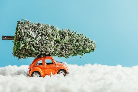 side view of toy vehicle with miniature christmas tree on rooftop riding by snow made of cotton on blue backgroundの写真素材