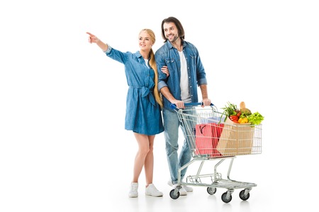 couple with shopping cart full of bags pointing at something isolated on whiteの写真素材