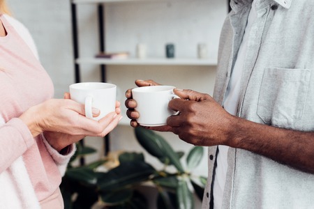 close up of woman and african american man holding white cups
