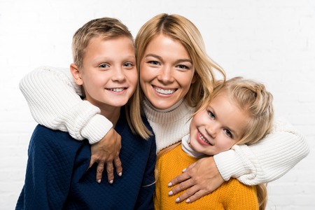 family portrait of happy mother hugging son and daughter looking at camera on white backgroundの写真素材