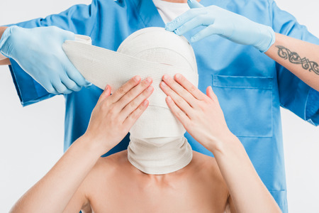 close up of plastic surgeon in gloves taping up woman face with bandage isolated on white