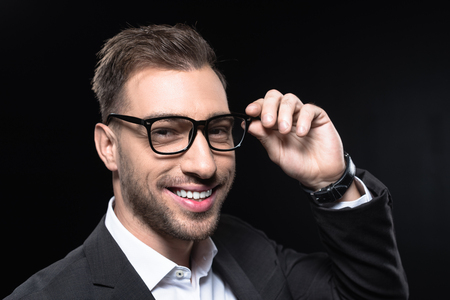 close-up portrait of handsome young businessman in eyeglasses looking at camera isolated on blackの写真素材