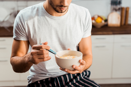 cropped shot of young man in pajamas eating cereals for breakfast at homeの写真素材