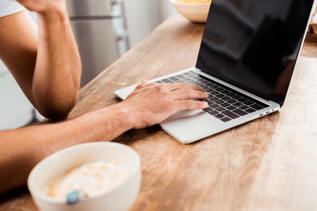 cropped shot of man using laptop with blank screen on kitchen table at morningの写真素材