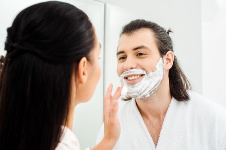 Woman applying shaving foam on smiling husband faceの写真素材