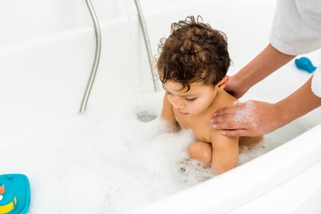 Female hands washing toddler boy in white bathroomの写真素材