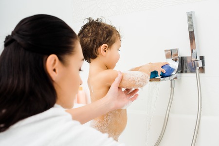 Mom holding hand of son playing in white bathroomの写真素材