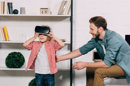 curly boy putting on virtual reality headset while his father sitting near at homeの写真素材