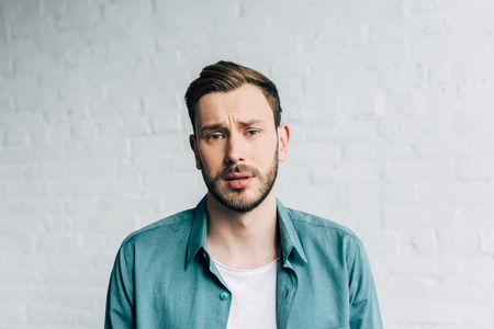 portrait of upset handsome man looking at camera in front of brick wall