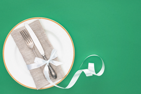 elevated view of plate with fork and knife wrapped by festive ribbon isolated on greenの写真素材
