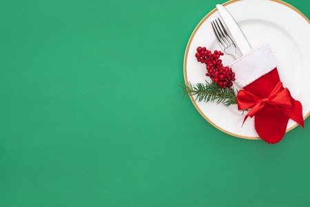 elevated view of red berries, evergreen tree branch and fork with knife in christmas sock on plate...