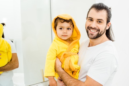 happy smiling father holding son in yellow bathrobeの写真素材