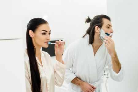 Beautiful woman cleaning teeth while husband shaving beardの写真素材