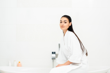 Attractive woman in bathrobe sitting in white bathroomの写真素材