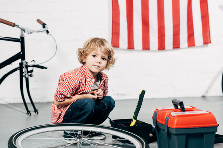 adorable little boy sitting near tools boxes near disassembled bicycle at workshopの写真素材