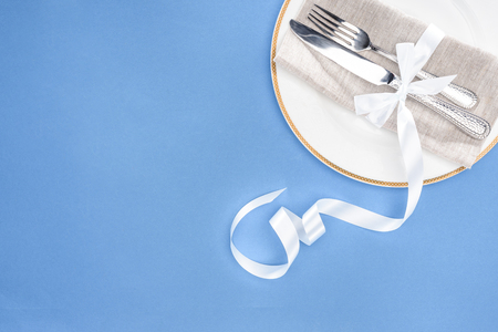 elevated view of fork and knife wrapped by festive ribbon on plate isolated on blueの写真素材