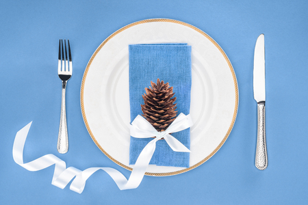 elevated view of plate with pine cone wrapped by festive ribbon and fork with knife isolated on blueの写真素材