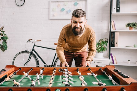smiling handsome adult man looking at camera and playing table football game at homeの写真素材