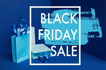 close up view of paper shopping bags arranged on blue backdrop with black friday sale