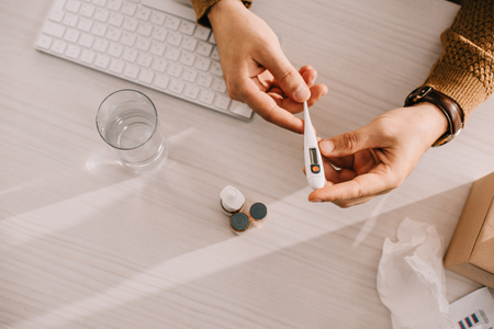 cropped view of businessman holding medical thermometer at office desk