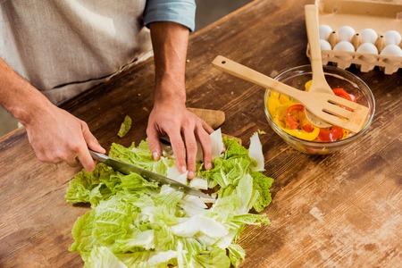 cropped shot of man in apron chopping cabbage and cooking vegetable saladの写真素材