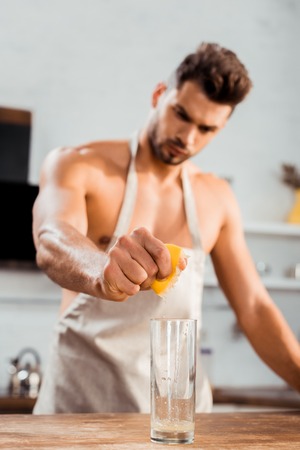 close-up view of bare-chested young man in apron squeezing lemon in glassの写真素材