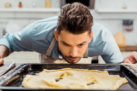 young man in apron looking at spoiled dough on baking trayの写真素材