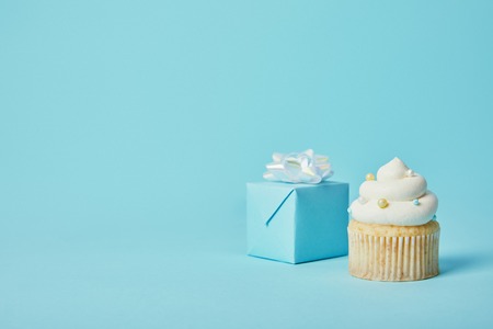 Gift box with white bow and delicious cupcake on blue backgroundの写真素材