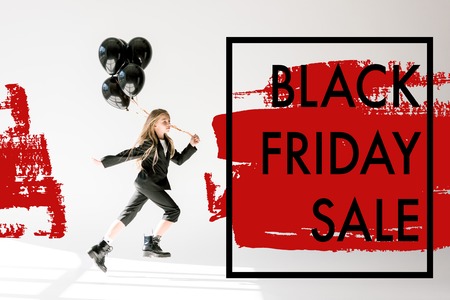 fashionable child in trendy suit jumping with black balloons on grey, black friday sale banner conceptの写真素材