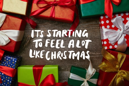 flat lay with christmas presents wrapped in different wrapping papers with ribbons on wooden surface with "its starting to feel a lot like christmas" inspirationの写真素材
