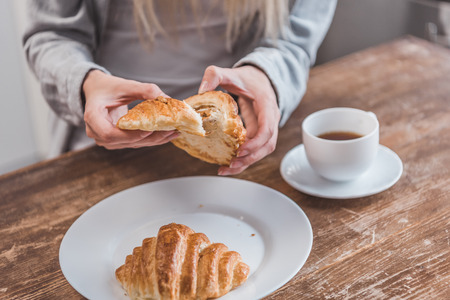 cropped view of female hands holding croissant at wooden tableの写真素材